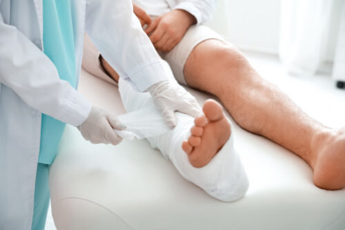 Doctor putting broken leg of young man in plaster